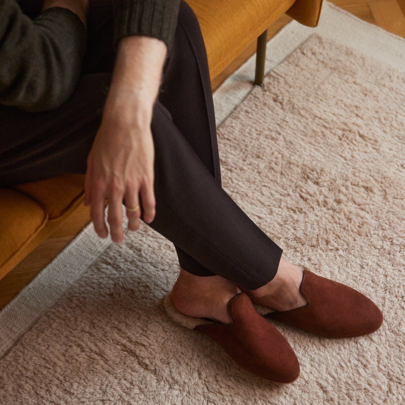 Inabo Men's Fritz Slipper in tobacco suede and white shearling worn by a man sitting on a couch