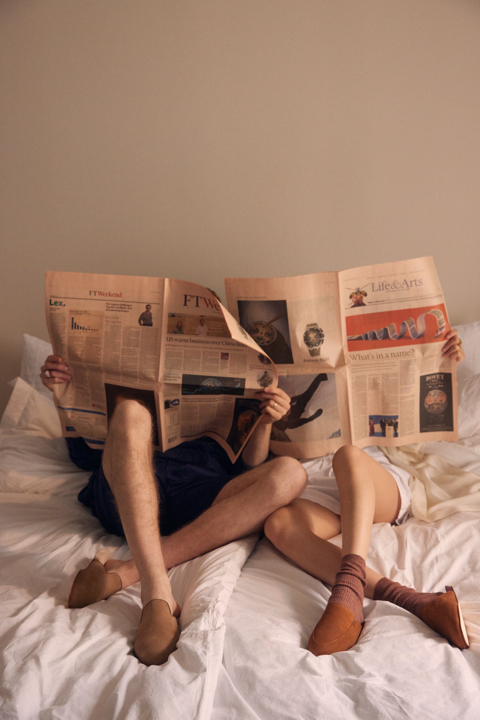 InaboMan and Woman sitting on a bed reading a paper magazine with Brown suede slippers on their feet