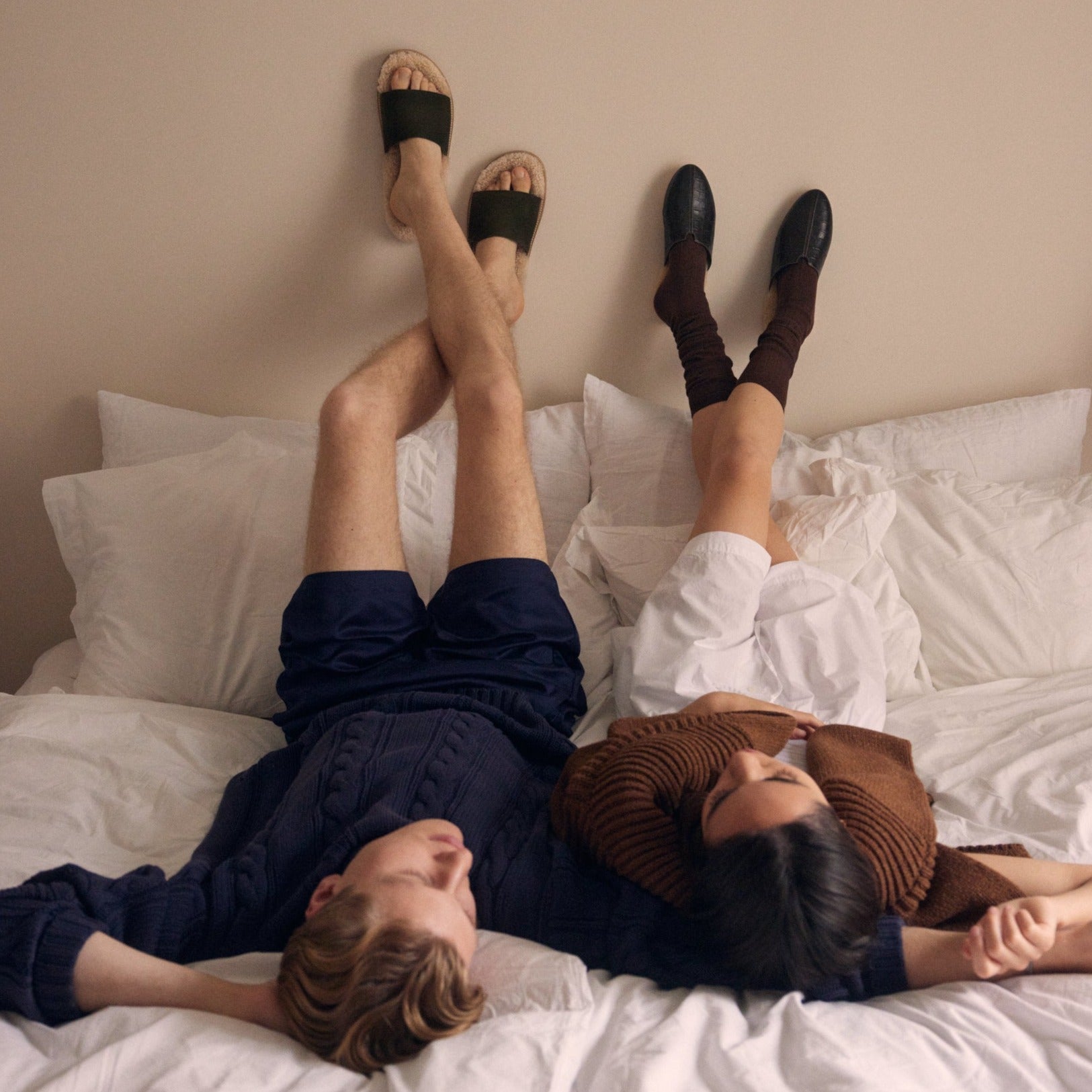 One man and a women lying in bed with their feet up on the wall wearing Inabo slippers 