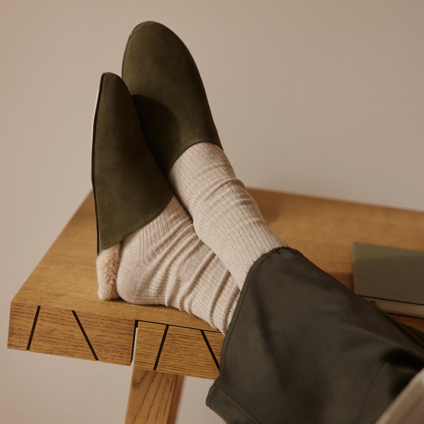 Inabo Men's Slider slippers in army suede and white shearling worn by a man with his feet up on a table