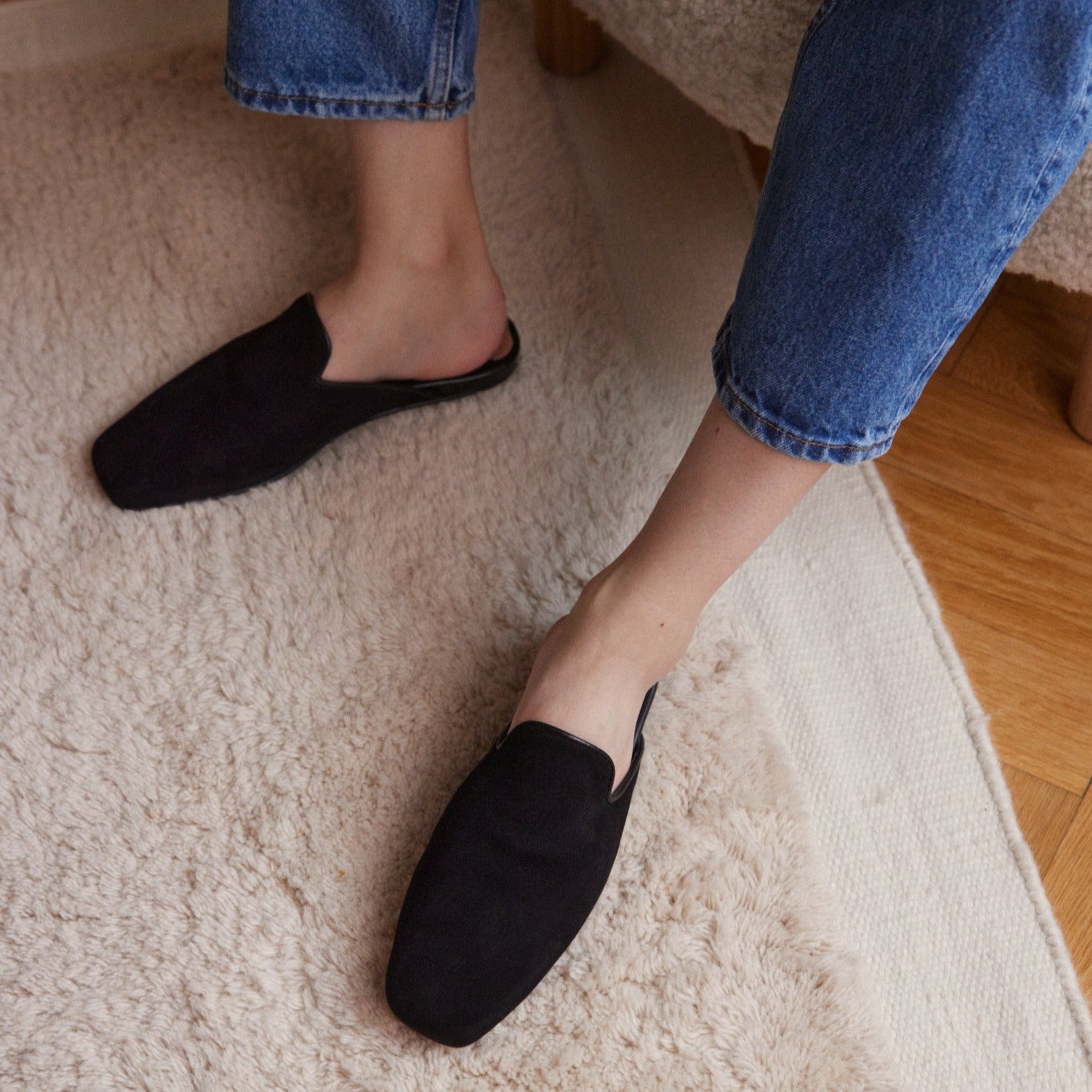 Inabo Women's Hilma slipper in black suede worn by women wearing blue jeans and standing on a white fluffy rug 